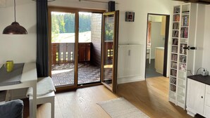 Une pièce chaleureuse avec un plancher en bois, un radiateur blanc, une bibliothèque et une porte-fenêtre coulissante donnant sur un espace extérieur.
