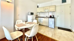 Cocina compacta con electrodomésticos blancos, un comedor con sillas blancas y una pequeña mesa.