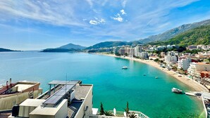 Un paisaje costero con mar azul cristalino, edificios a lo largo de la orilla y montañas al fondo.