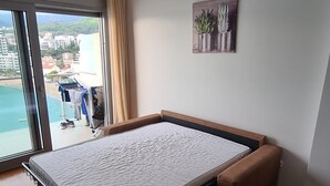Un dormitorio con cama abatible, vista a un balcón con ropa tendida y una planta en maceta en la pared.