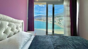 Un dormitorio con una cama grande, vistas a una ciudad costera y un balcón con cortinas.