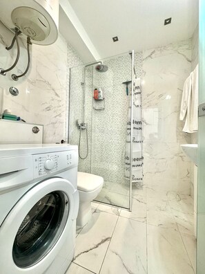 A modern bathroom with a built-in washing machine, a glass shower enclosure, and a toilet.