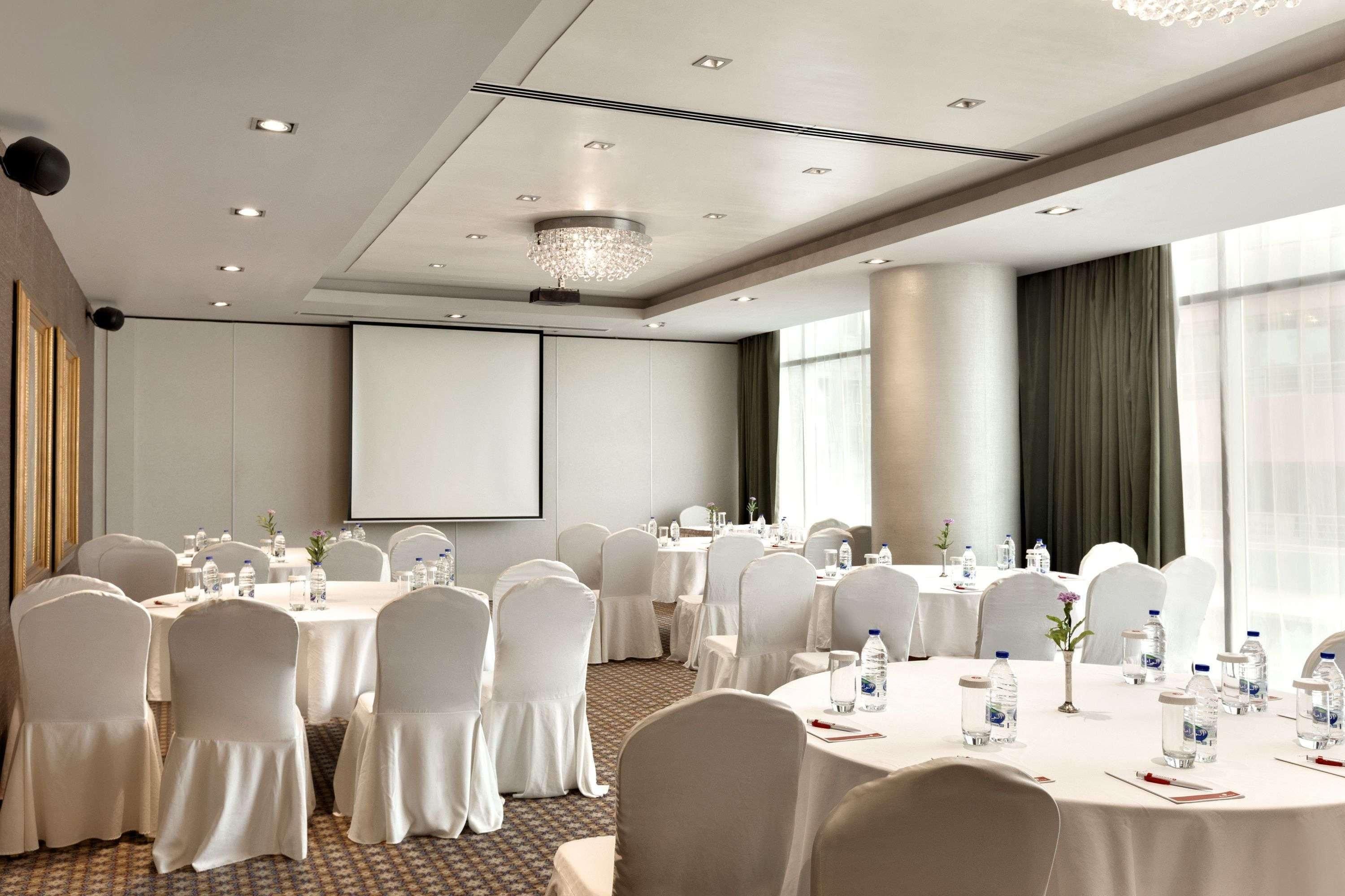 A conference room with round tables, white chairs, and a projector screen.