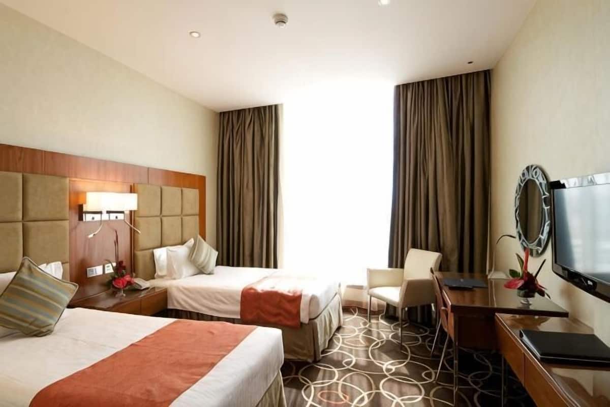 Habitación de hotel con dos camas, un escritorio, una silla, un televisor y un ventanal con cortinas.