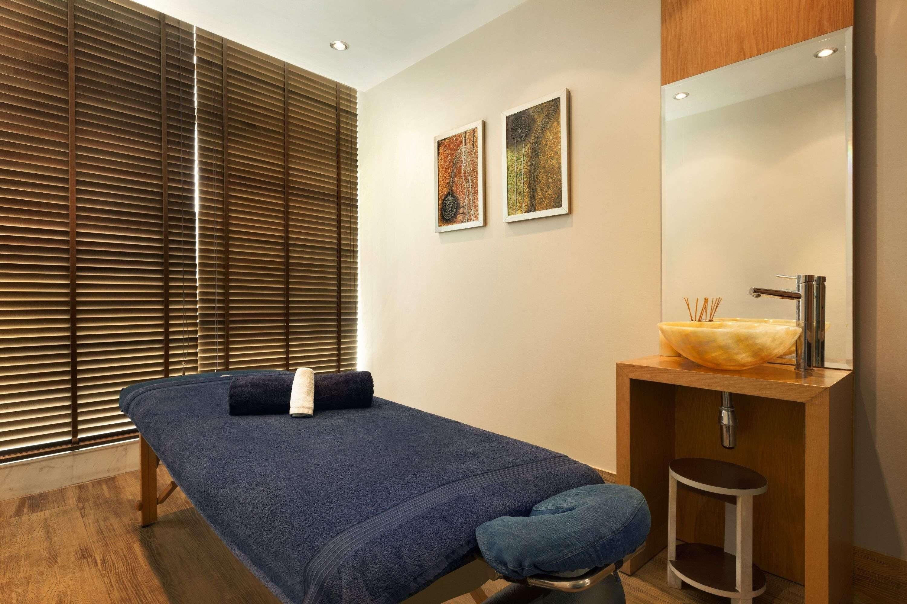A room with a massage table, a wooden bench, a sink with a bowl, and two framed artworks on the wall.