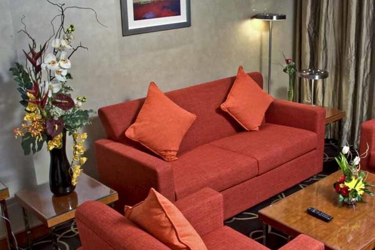 Un canapé rouge avec des coussins assortis, un vase de fleurs et un tableau accroché au mur.