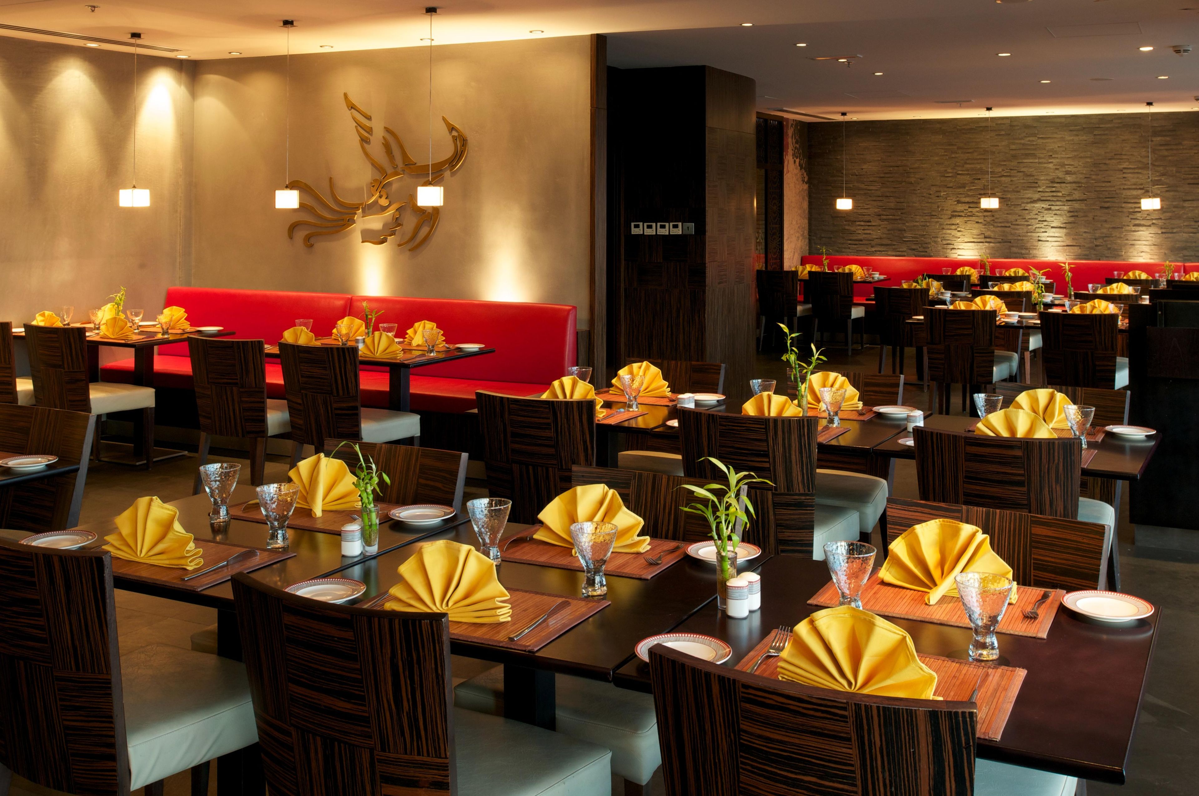 A restaurant with multiple dining tables, each set with yellow napkins, clear glassware, and wooden chairs.