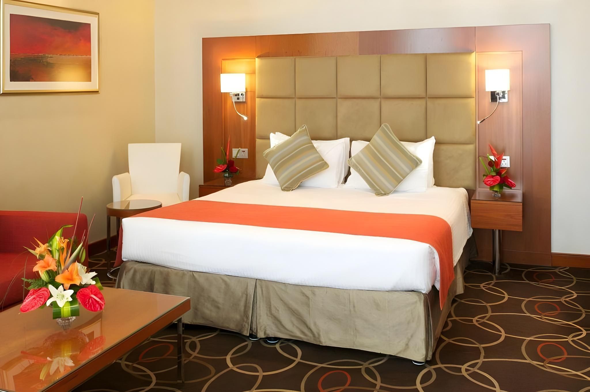 Une chambre d’hôtel avec un grand lit, un bureau, une chaise et un vase de fleurs.
