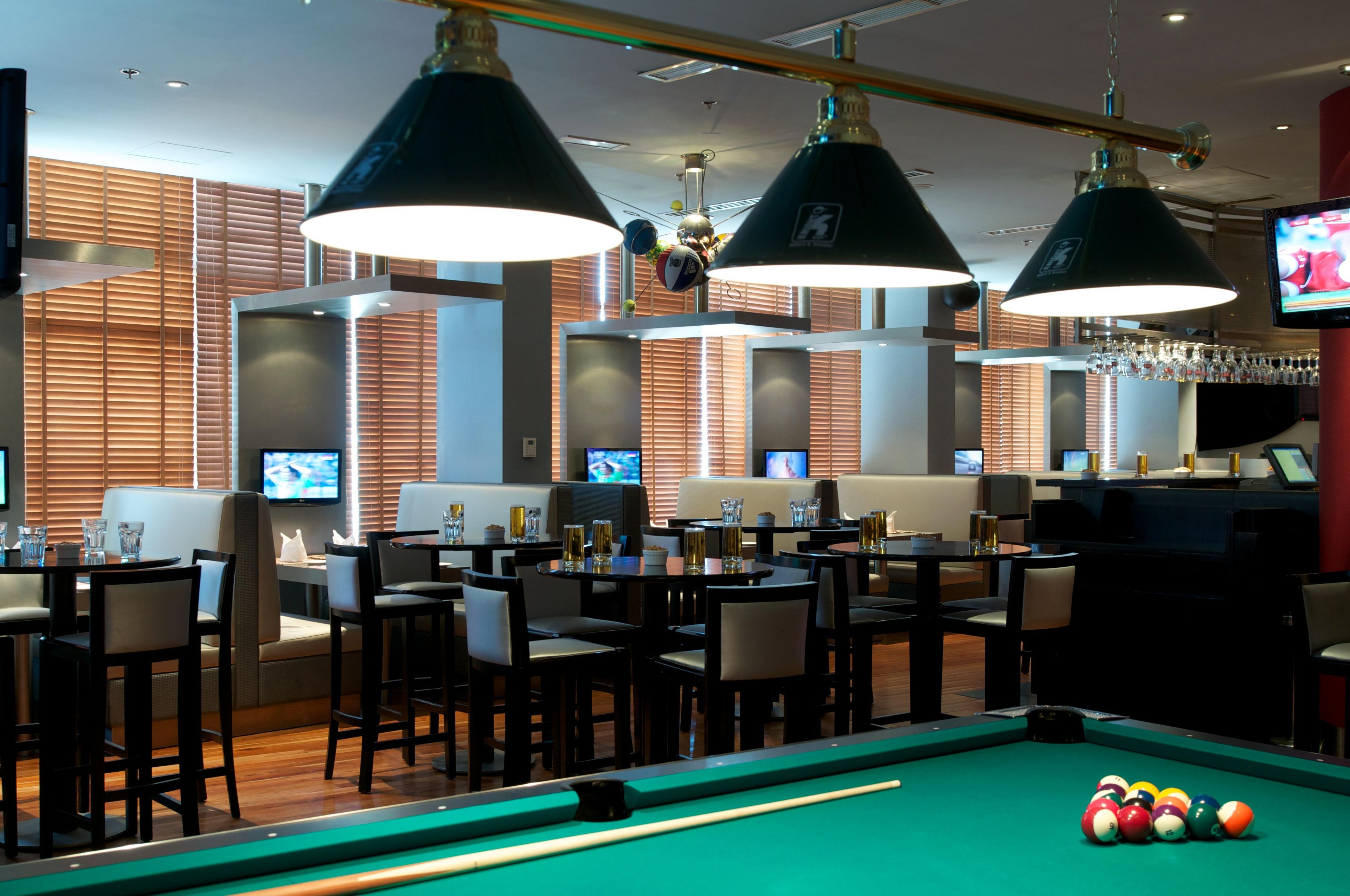 A billiards room with tables, chairs, and overhead lighting.