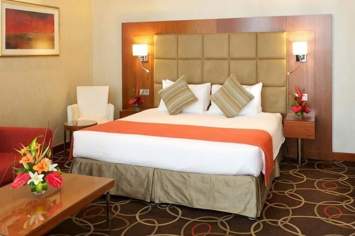 Una habitación de hotel con una cama grande, dos mesitas de noche, una silla y un escritorio con un jarrón de flores.