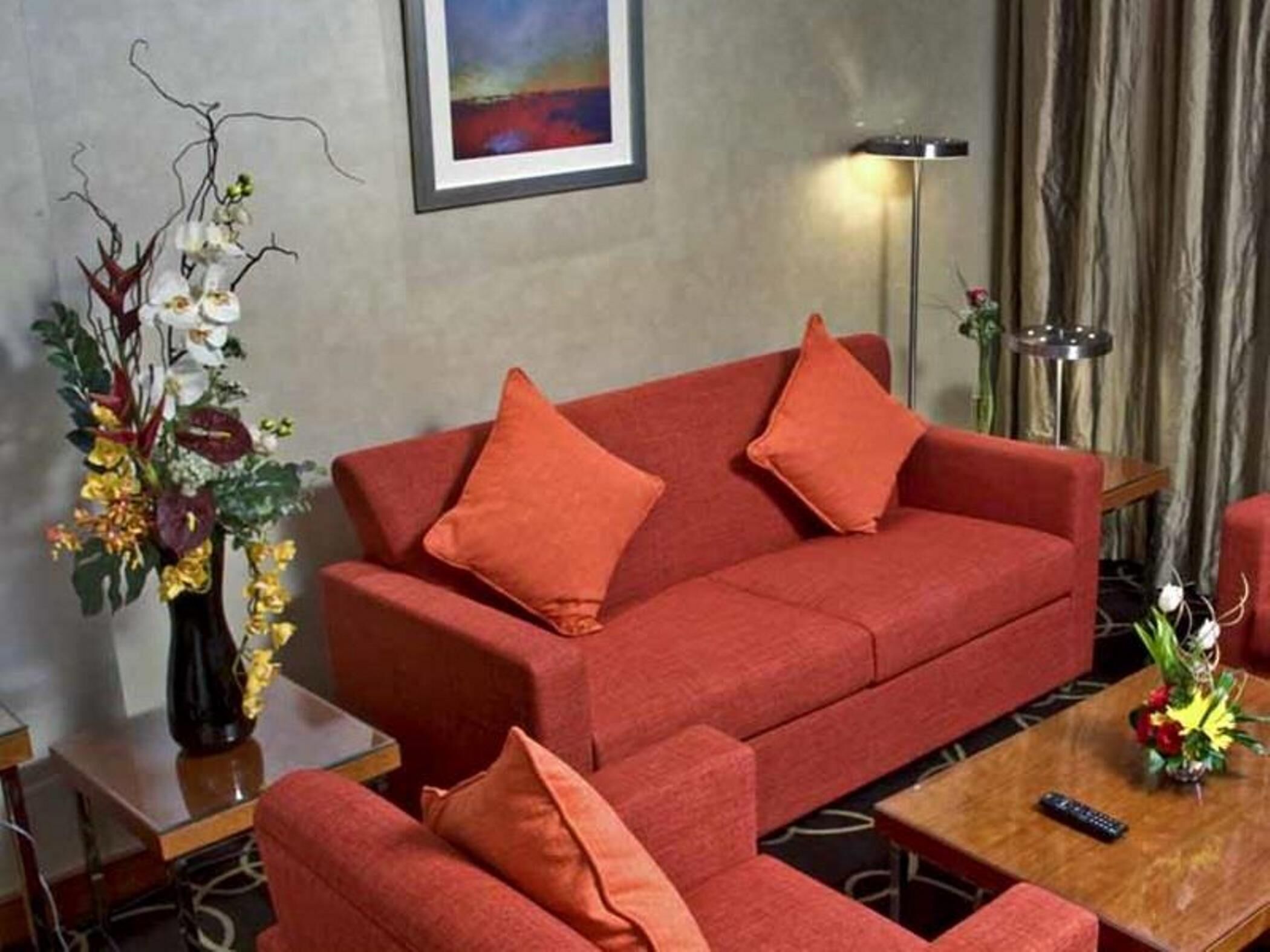 Ein rotes Sofa mit passenden Kissen, eine Blumenvase und ein Bild an der Wand.