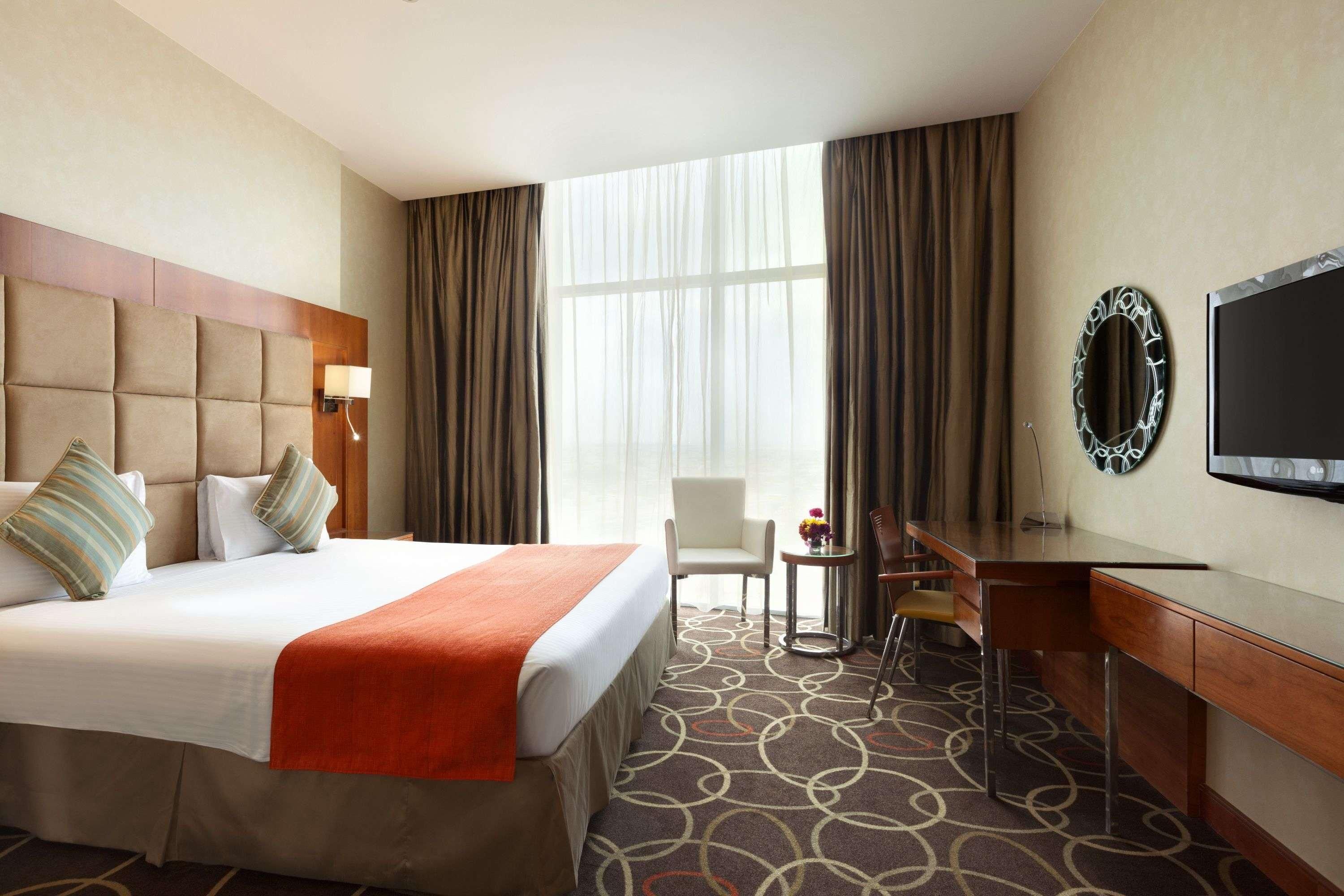 A hotel room with a large bed, a desk, a chair, a television, and a window with curtains.
