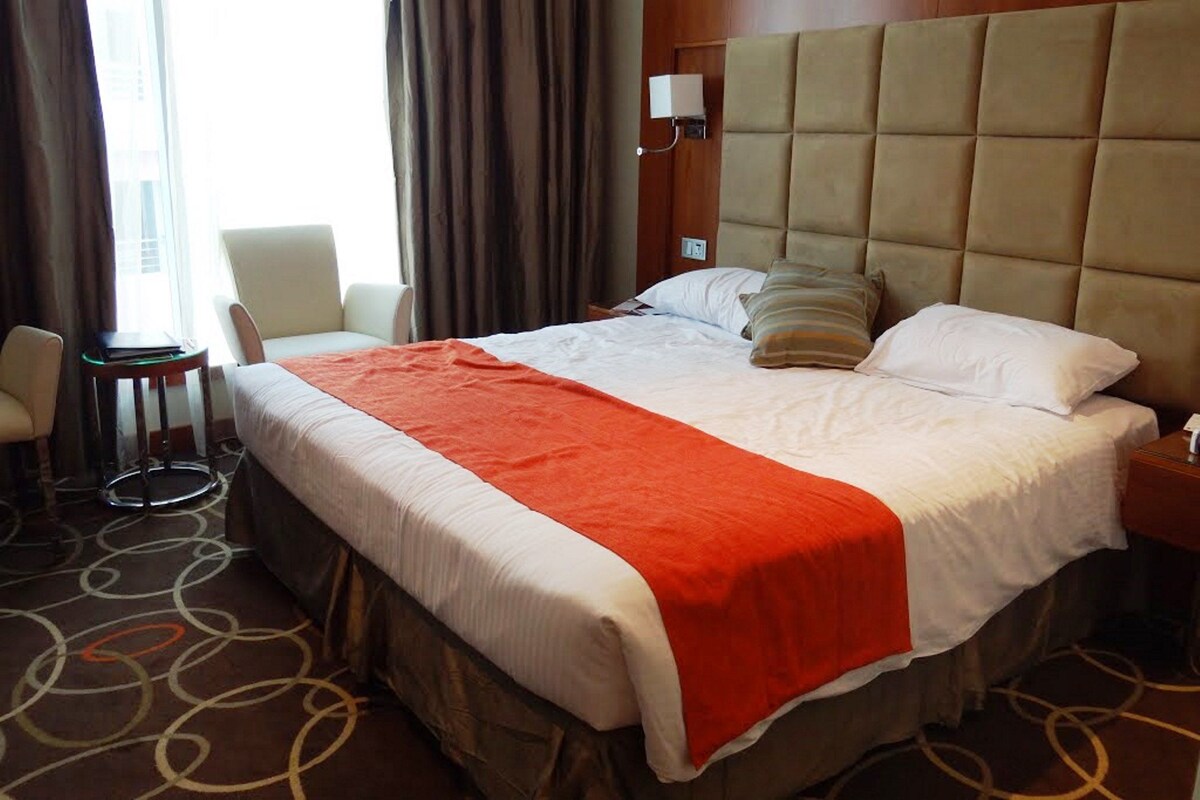 A hotel room with a large bed, a bedside table, a chair, and a small table.