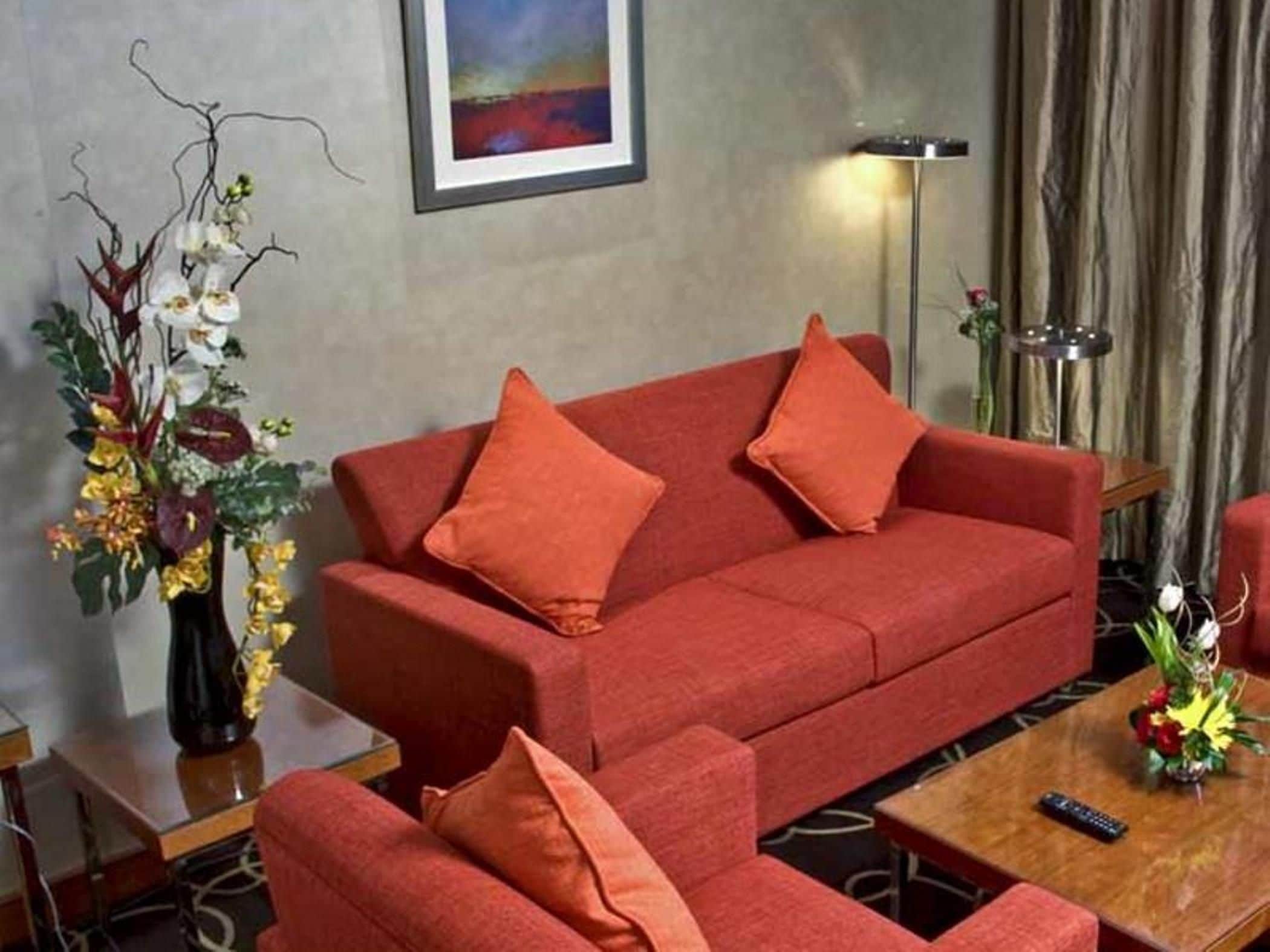 A red sofa with matching cushions, a vase of flowers, and a painting on the wall.