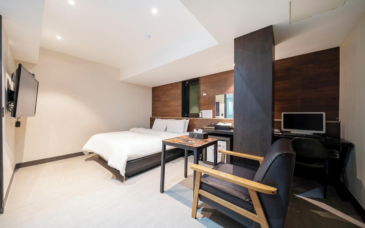 A modern hotel room with a bed, desk, chair, TV, and a large mirror.