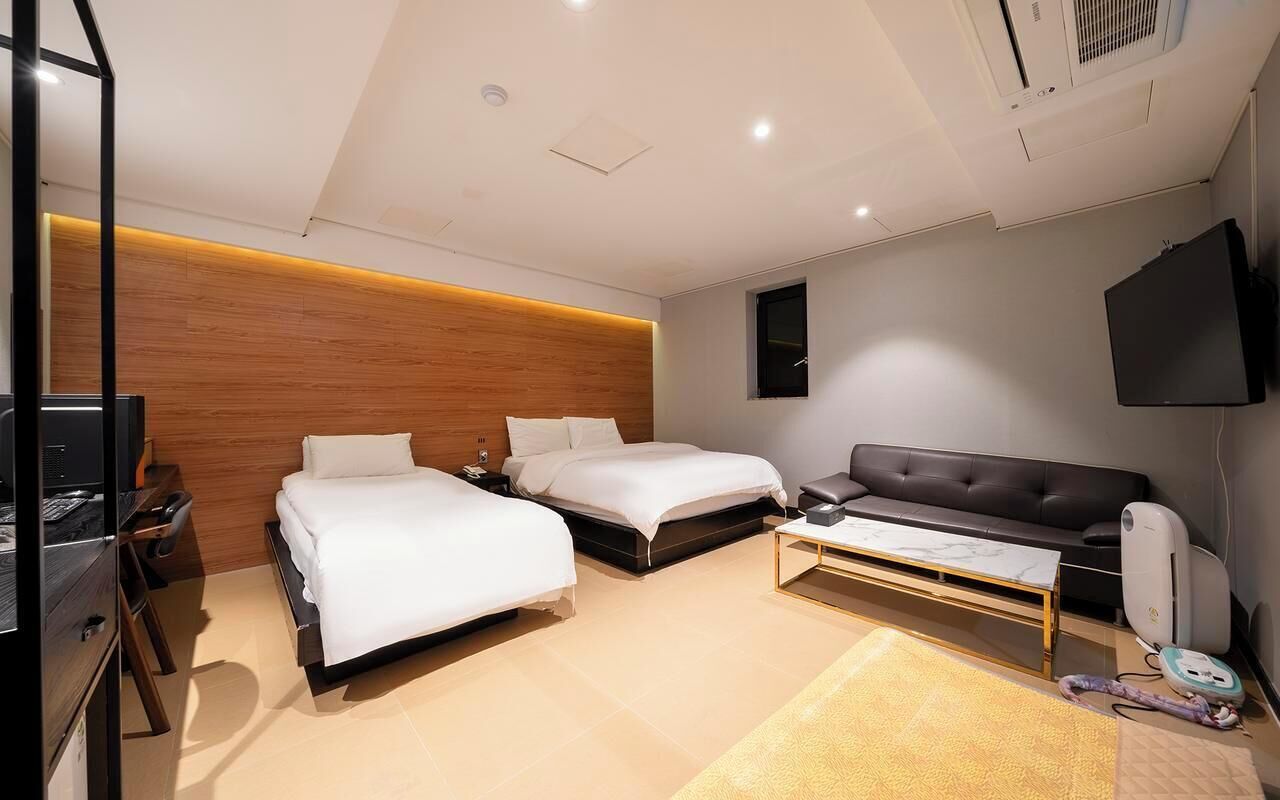 A modern hotel room with two beds, a flat-screen TV, a sofa, and a desk.