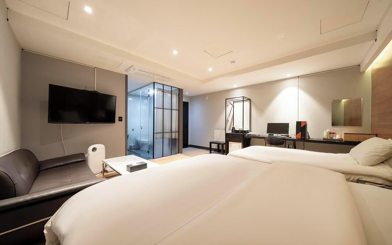 A hotel room with a bed, a desk, a chair, a TV, and a large window.