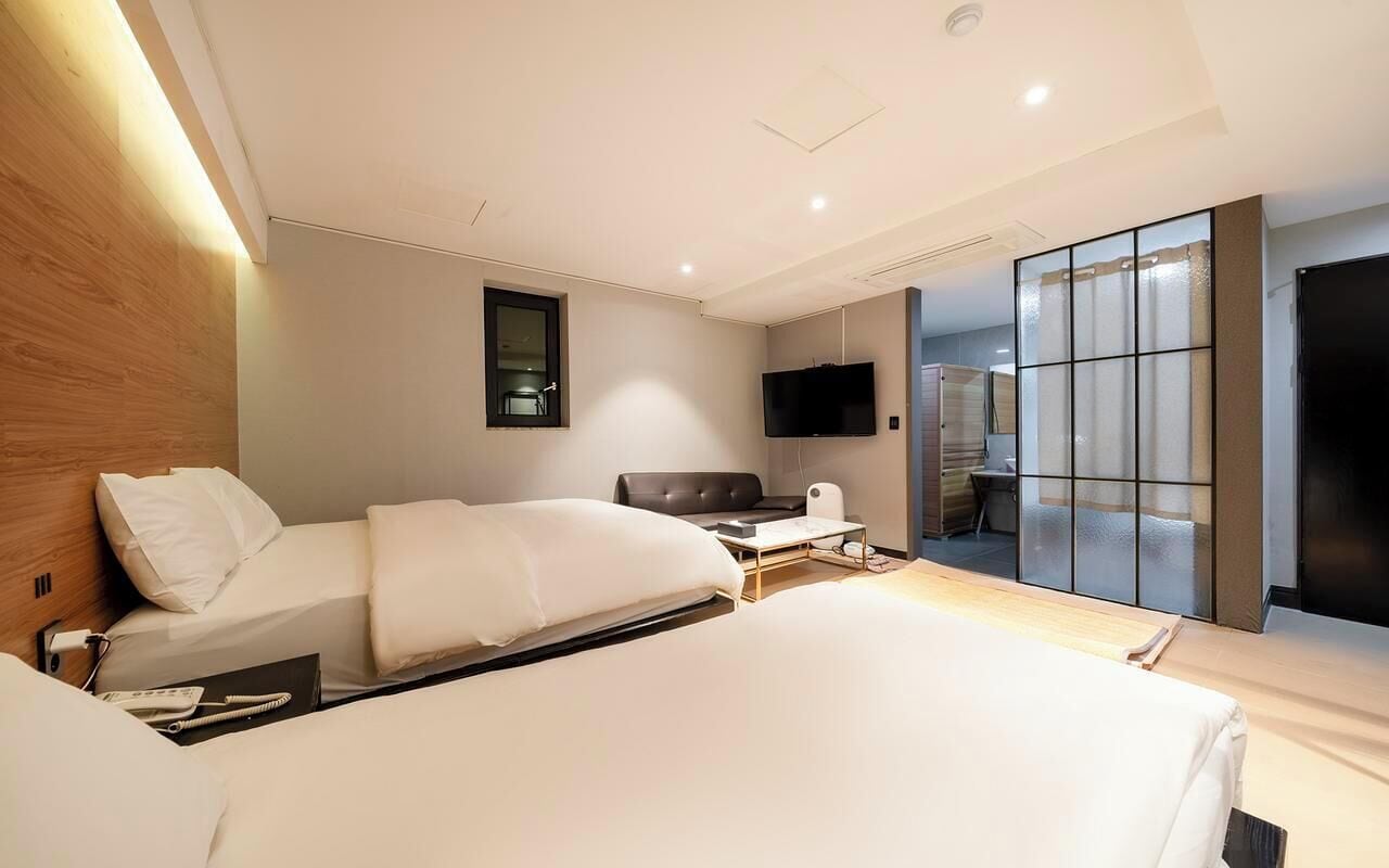 A hotel room with two beds, a seating area, a television, and a large window.