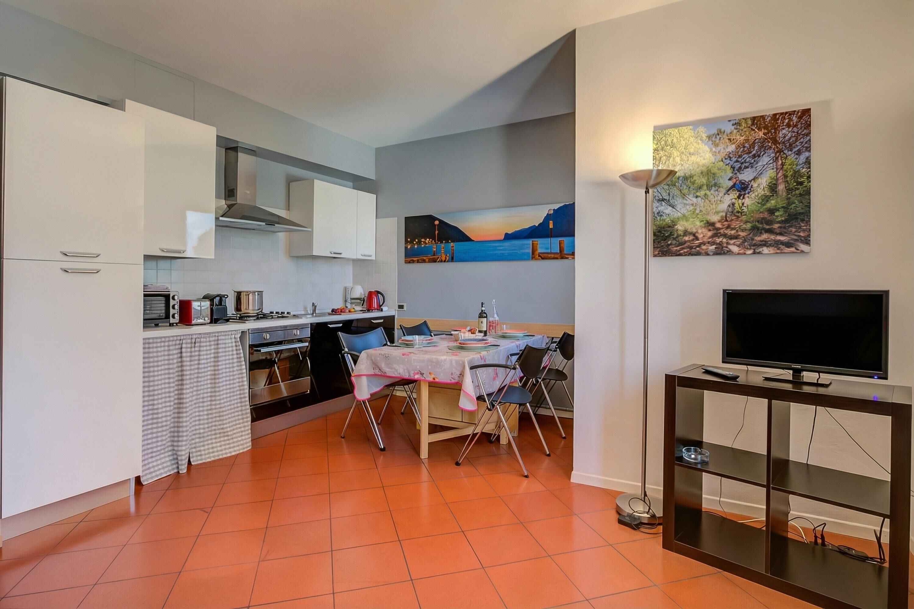 Een compacte keuken met moderne apparatuur, een eethoek met een tafel en stoelen, en een televisie op een standaard.