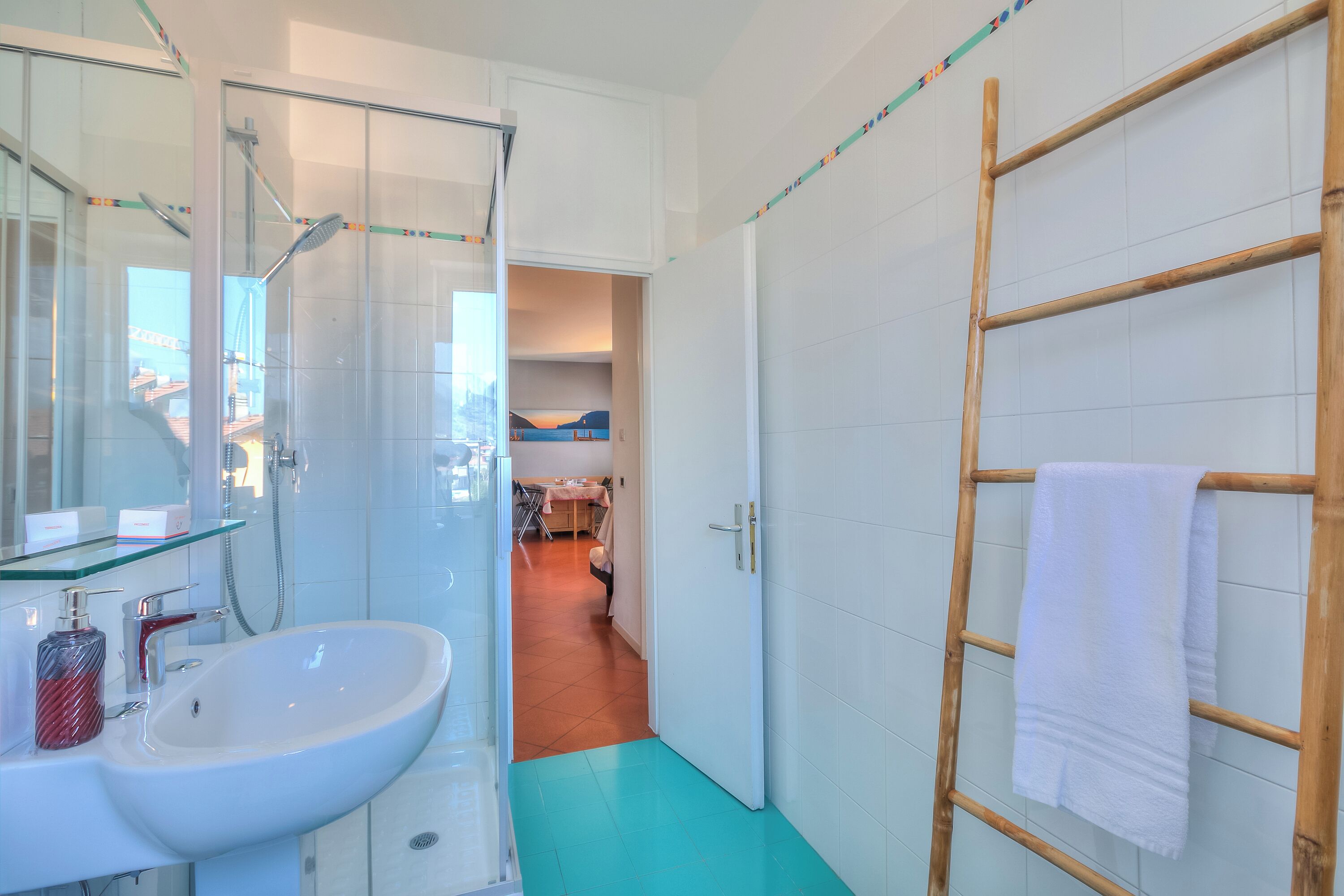 A bathroom with a white sink, mirror, and shower. There is a wooden ladder with a towel hanging on it.