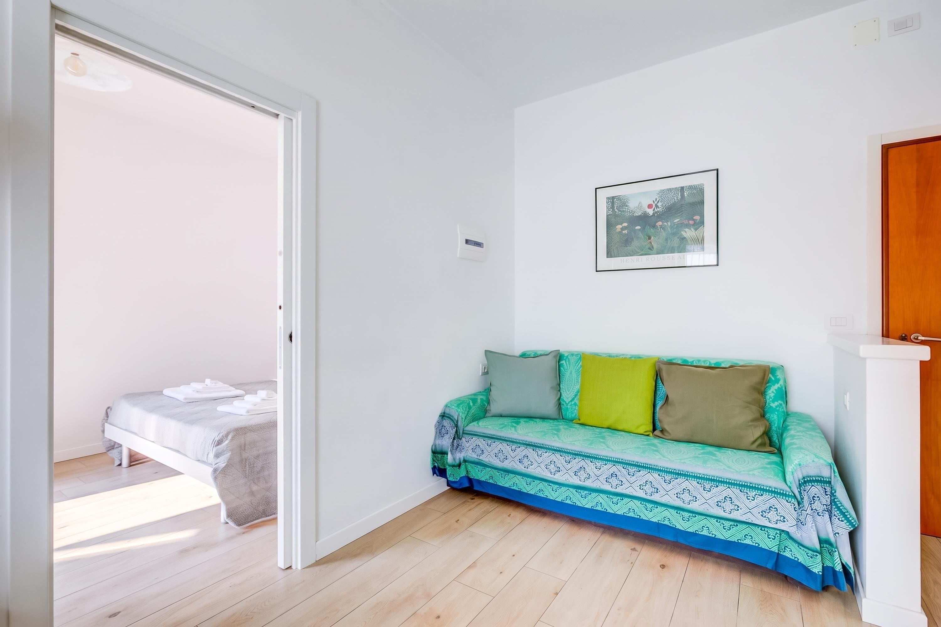 Een kamer met een bed, een groene sofa met patroon, een ingelijst schilderij aan de muur en een houten vloer.