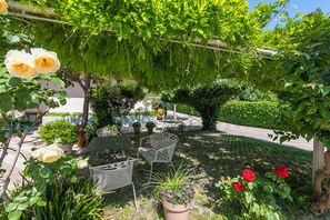 A garden patio with outdoor seating, a pergola, and various plants. - Casa al Cor Apartments (Nago-Torbole)