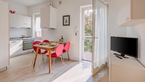 A modern kitchen with white cabinets, a dining table with red chairs, a TV, and a balcony with a view. - Casa al Cor Apartments (Nago-Torbole)