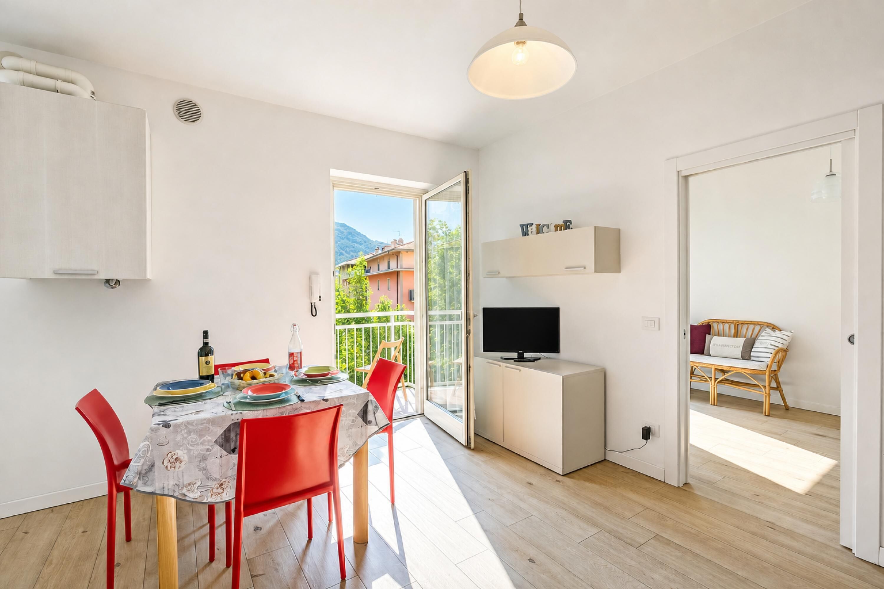 Un apartamento moderno con zona de comedor, televisor y balcón con vistas a edificios y montañas.