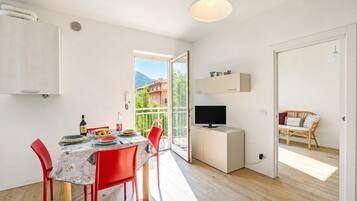 Un apartamento moderno con zona de comedor, televisor y balcón con vistas a edificios y montañas.