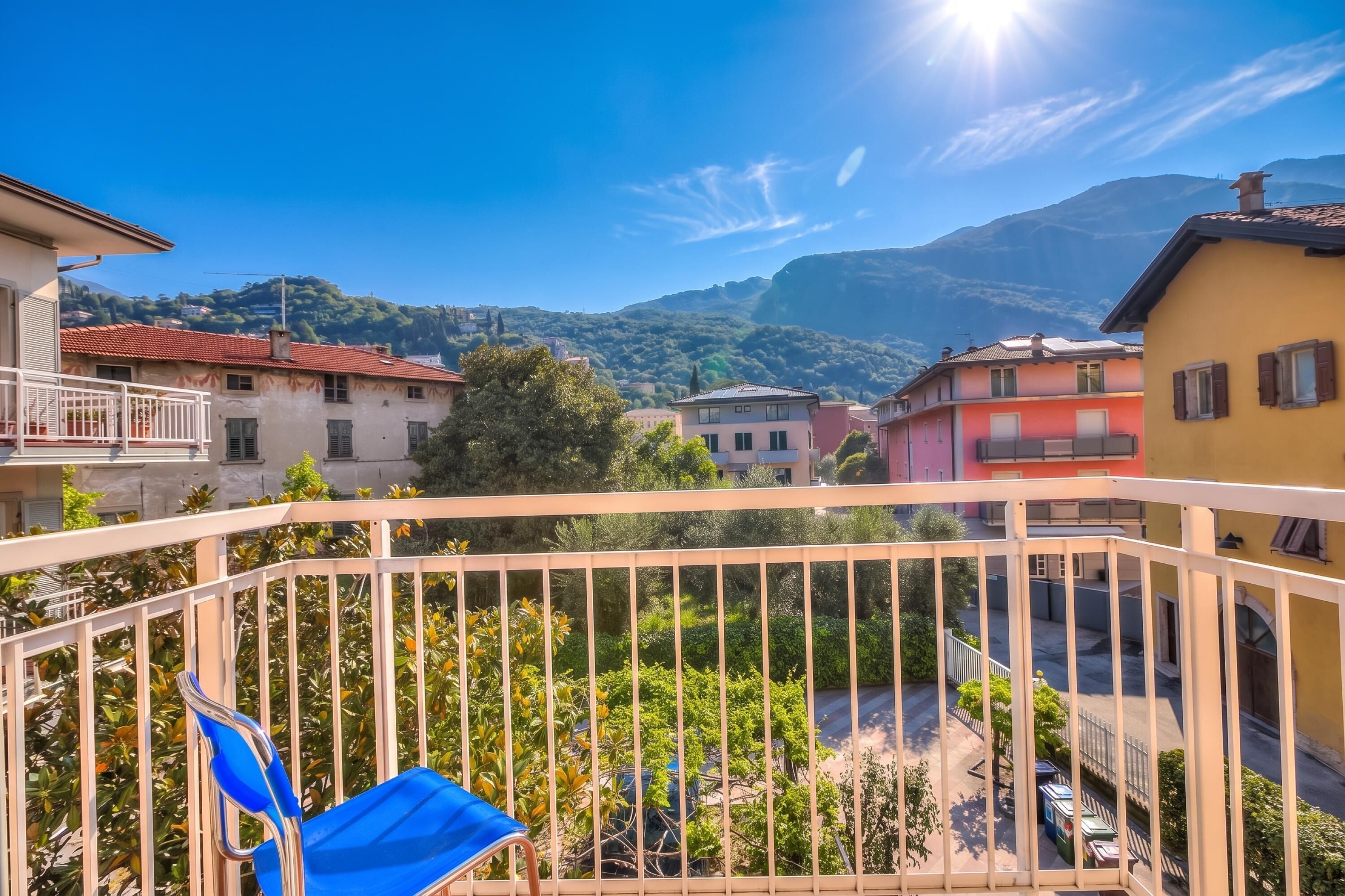A balcony with a blue chair, a view of a residential area with colorful buildings, and mountains in the background.