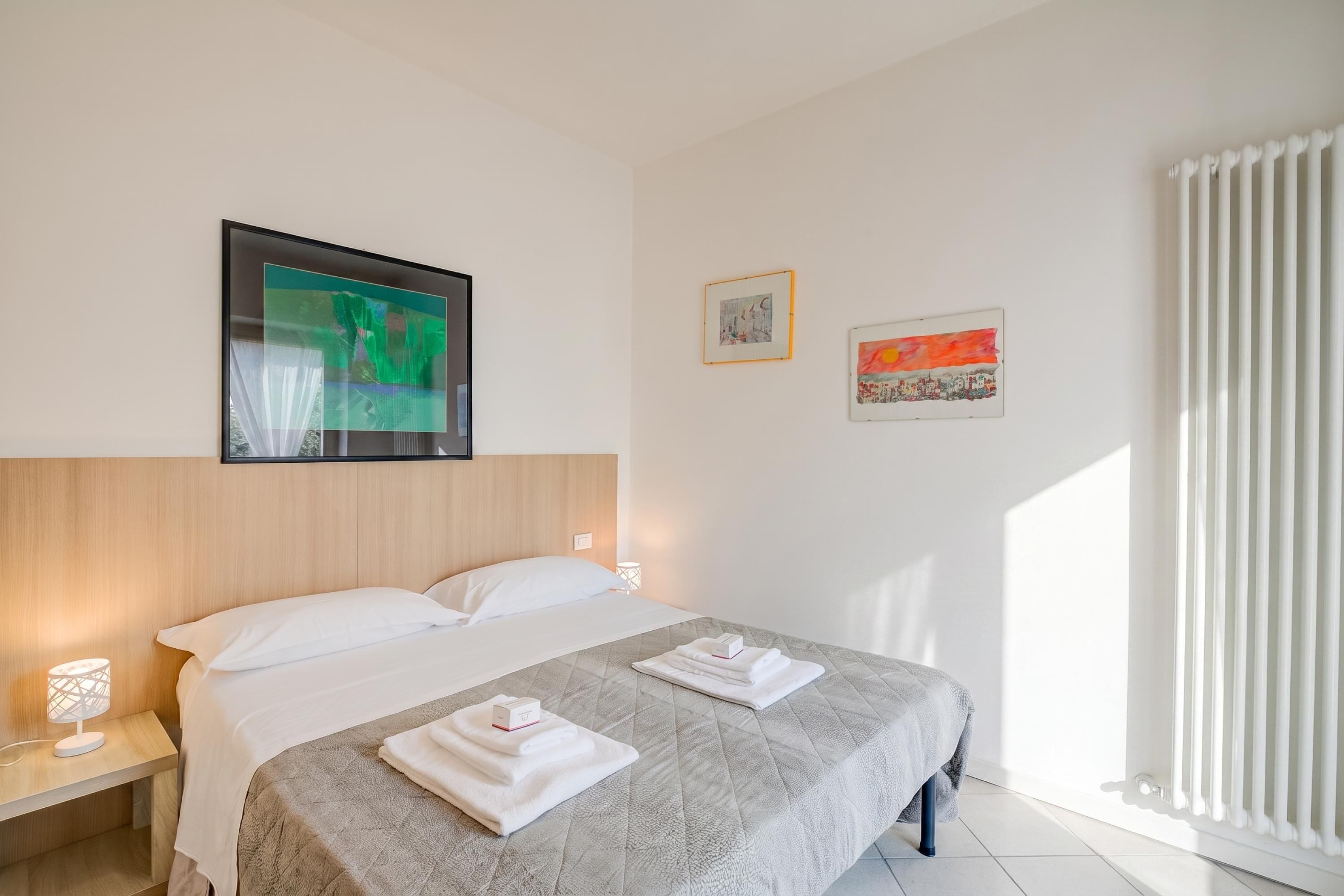 A hotel room with a bed, a nightstand, a lamp, and artwork on the walls.