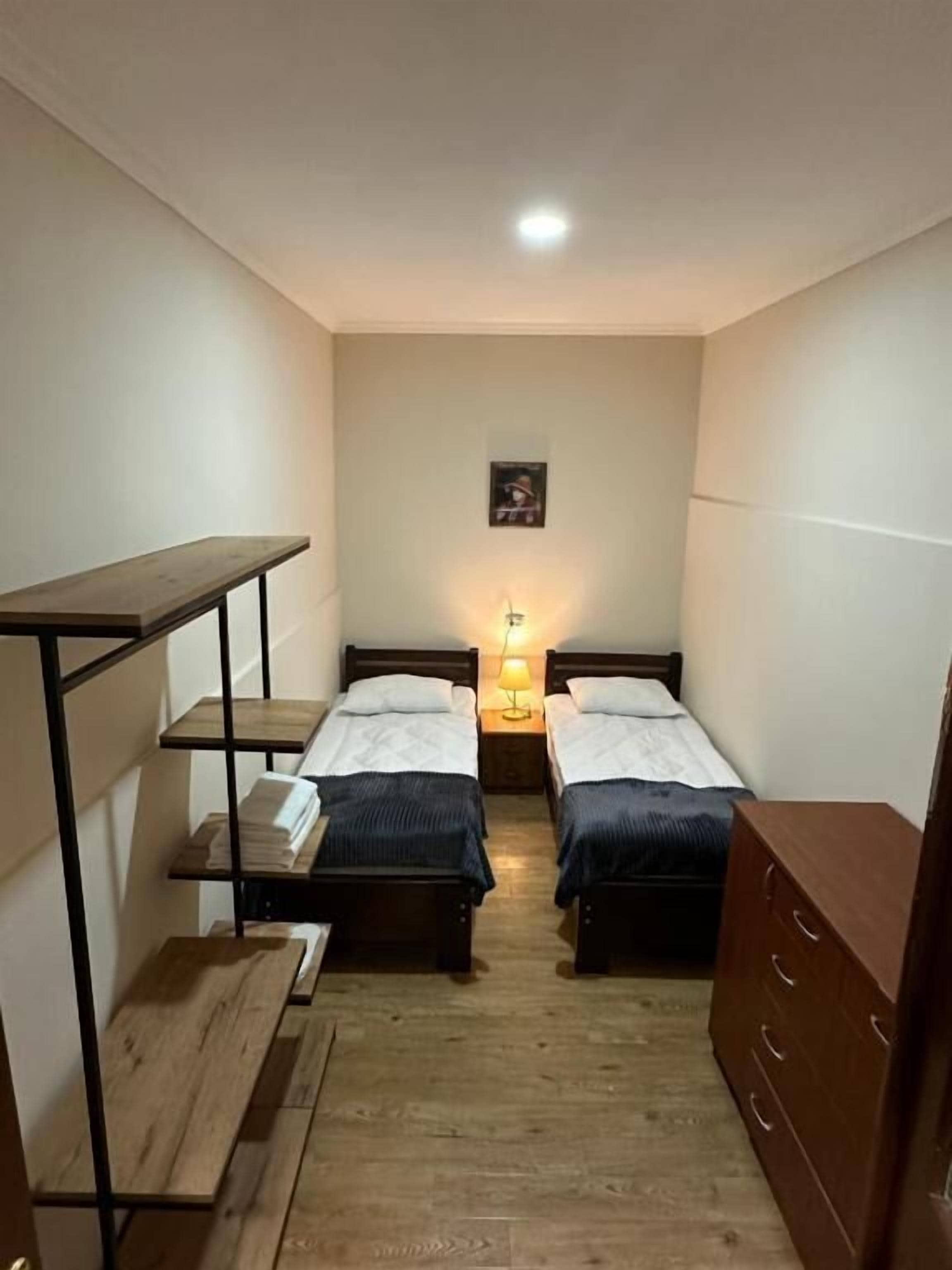 A small, narrow room with two single beds, a wooden bench, a small table, and a dresser.