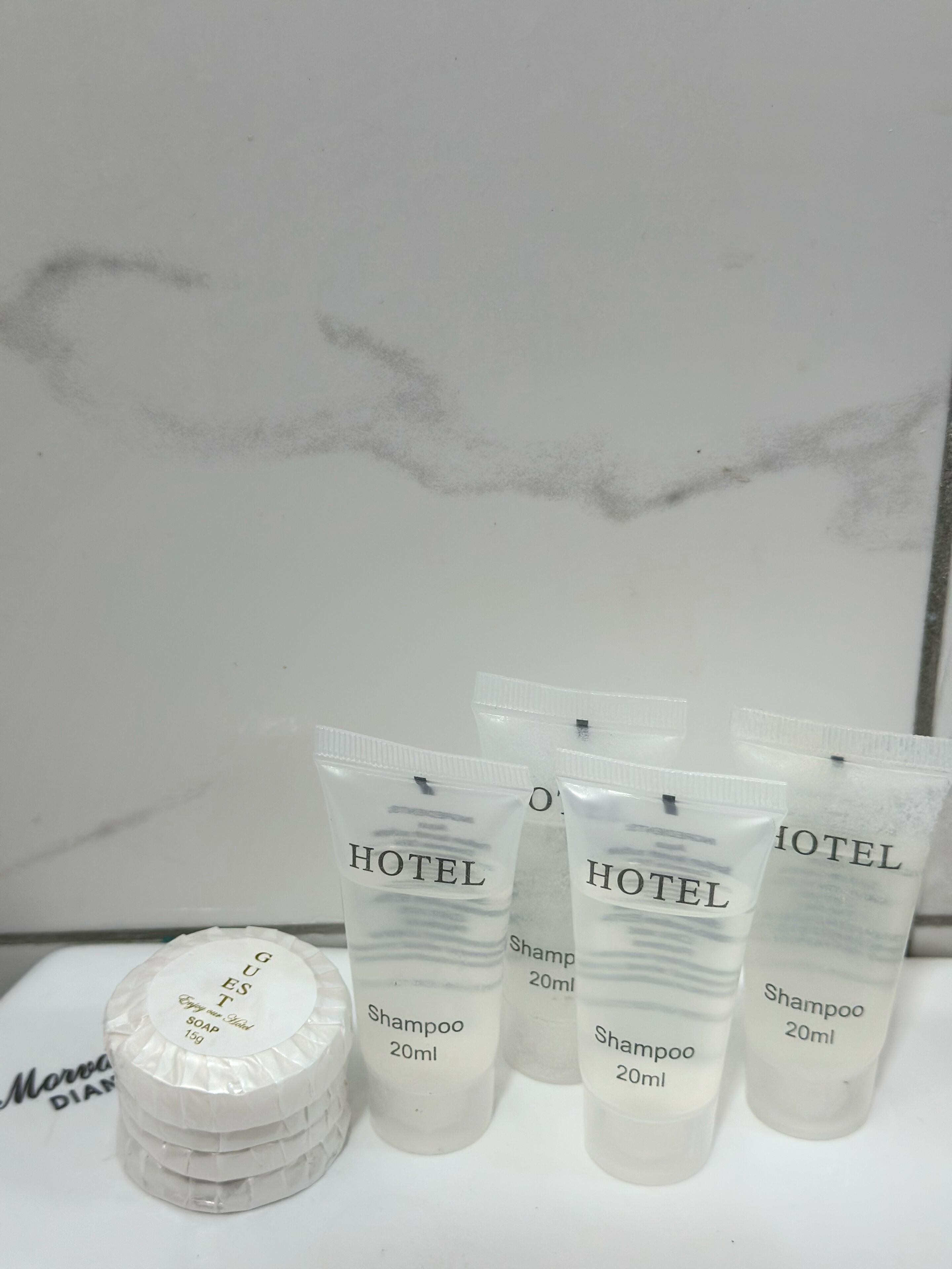Four 20ml hotel shampoo bottles and a stack of soap bars with a label that reads "Hotel Shampoo 20ml" and "Happy hotel soap 150g".