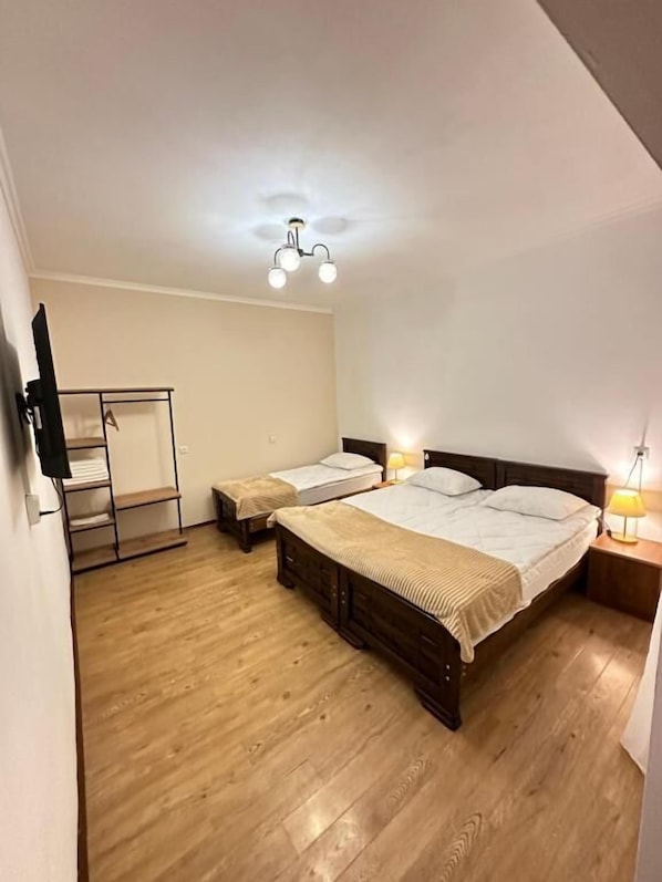 A bedroom with a large bed, two smaller beds, a wardrobe, and a ceiling light fixture.