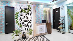 A reception area with a floral wallpaper, a white decorative panel, a reception desk, and a clock on the wall. - Mansavi Villa HomeStay (Greater Noida)