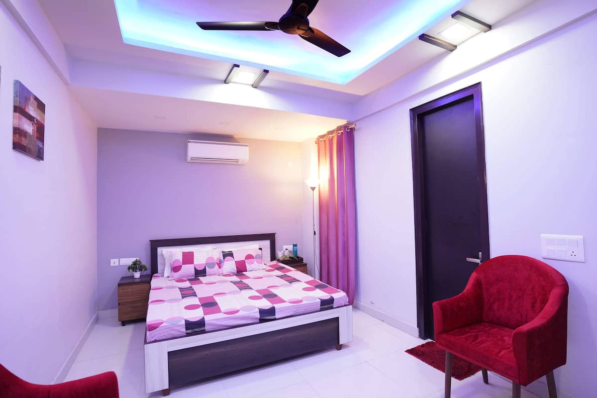 Une chambre à coucher moderne avec un lit, une chaise rouge et un ventilateur de plafond.
