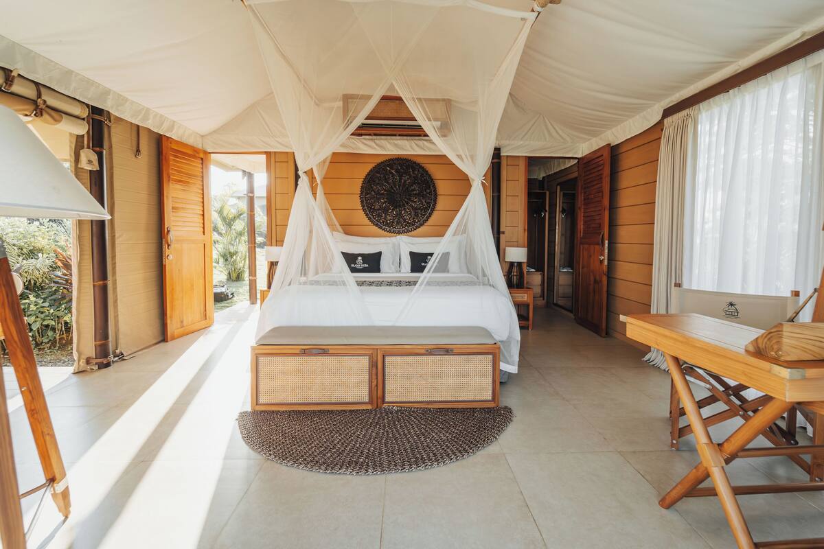 A tented room with a bed, wooden furniture, and a view of the outdoors.
