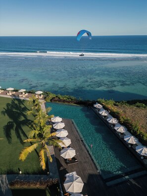 A resort with a clear view of the ocean, a pool area with umbrellas, and a parasail in the distance. - Glamp Nusa (Nusa Dua)