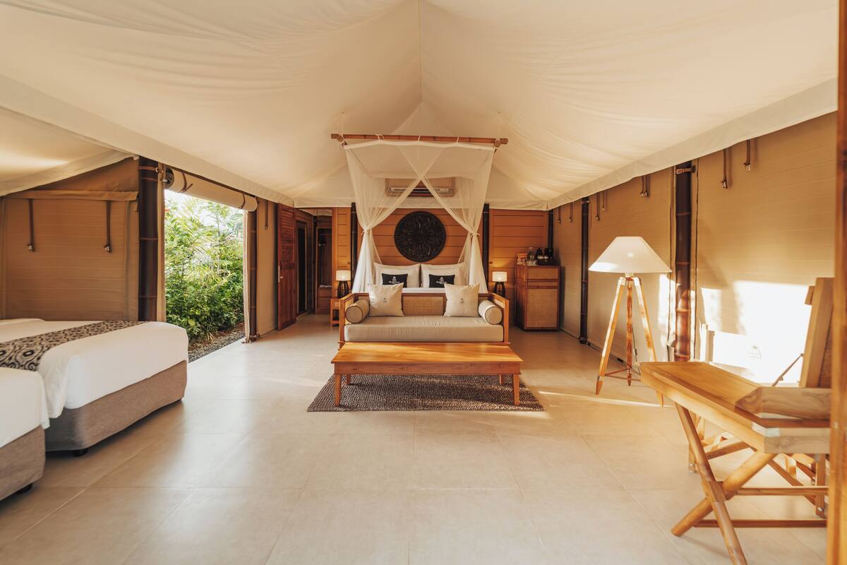 A spacious tented room with a large bed, a sofa, a wooden table, and a lamp.