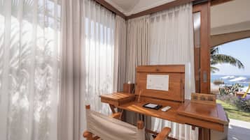 Una habitación con un escritorio de madera, una silla, un ventanal con cortinas traslúcidas y vista al océano.
