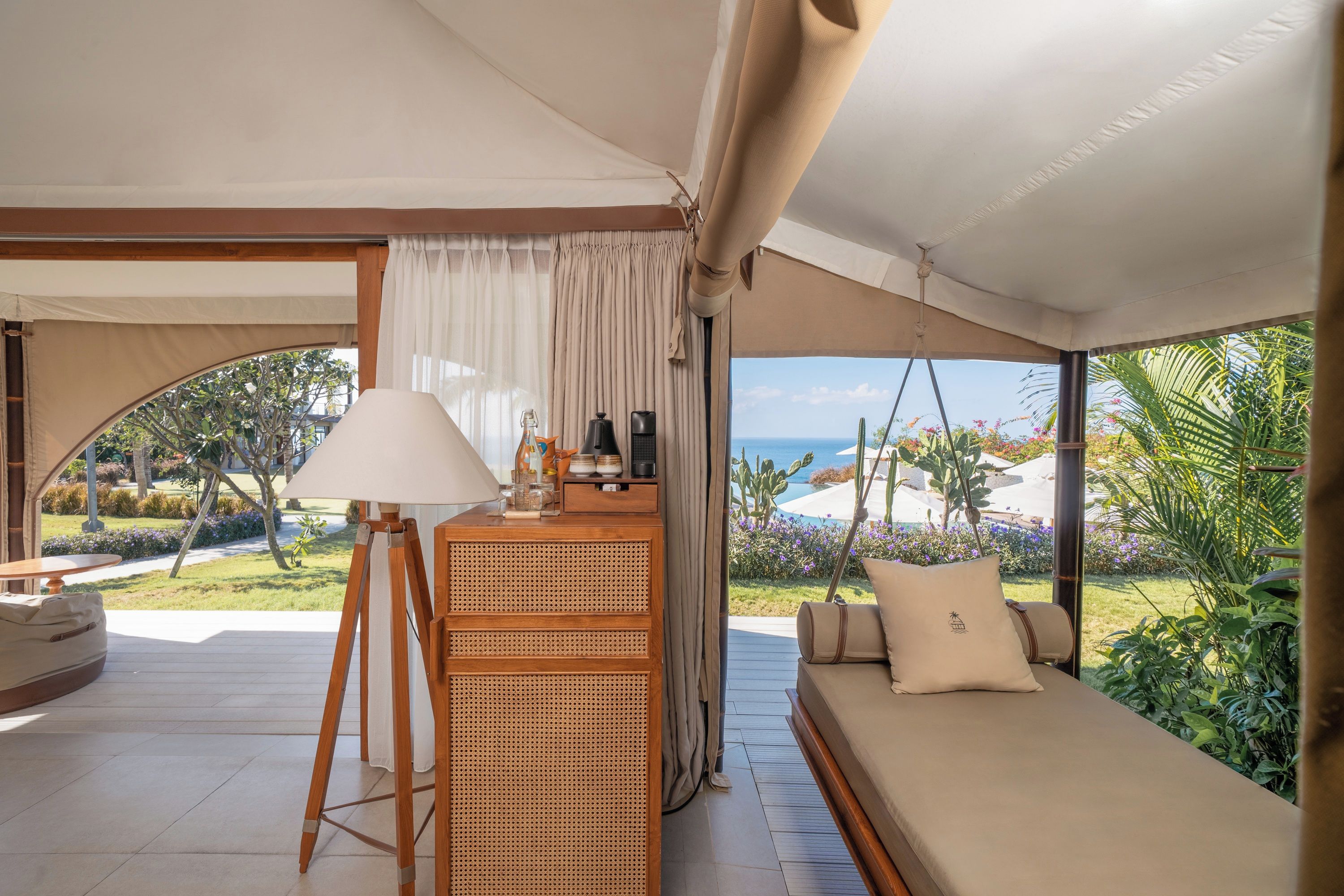 A tented room with a rattan desk, a sofa with cushions, and a view of the outdoors.