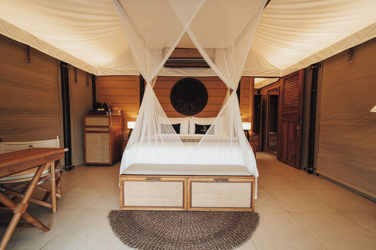 A bedroom with a canopy bed, wooden walls, a rattan headboard, and a round decorative wall piece.