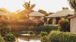 A serene garden with a pond, surrounded by lush greenery and a small building with a covered patio. - Glamp Nusa (Nusa Dua)