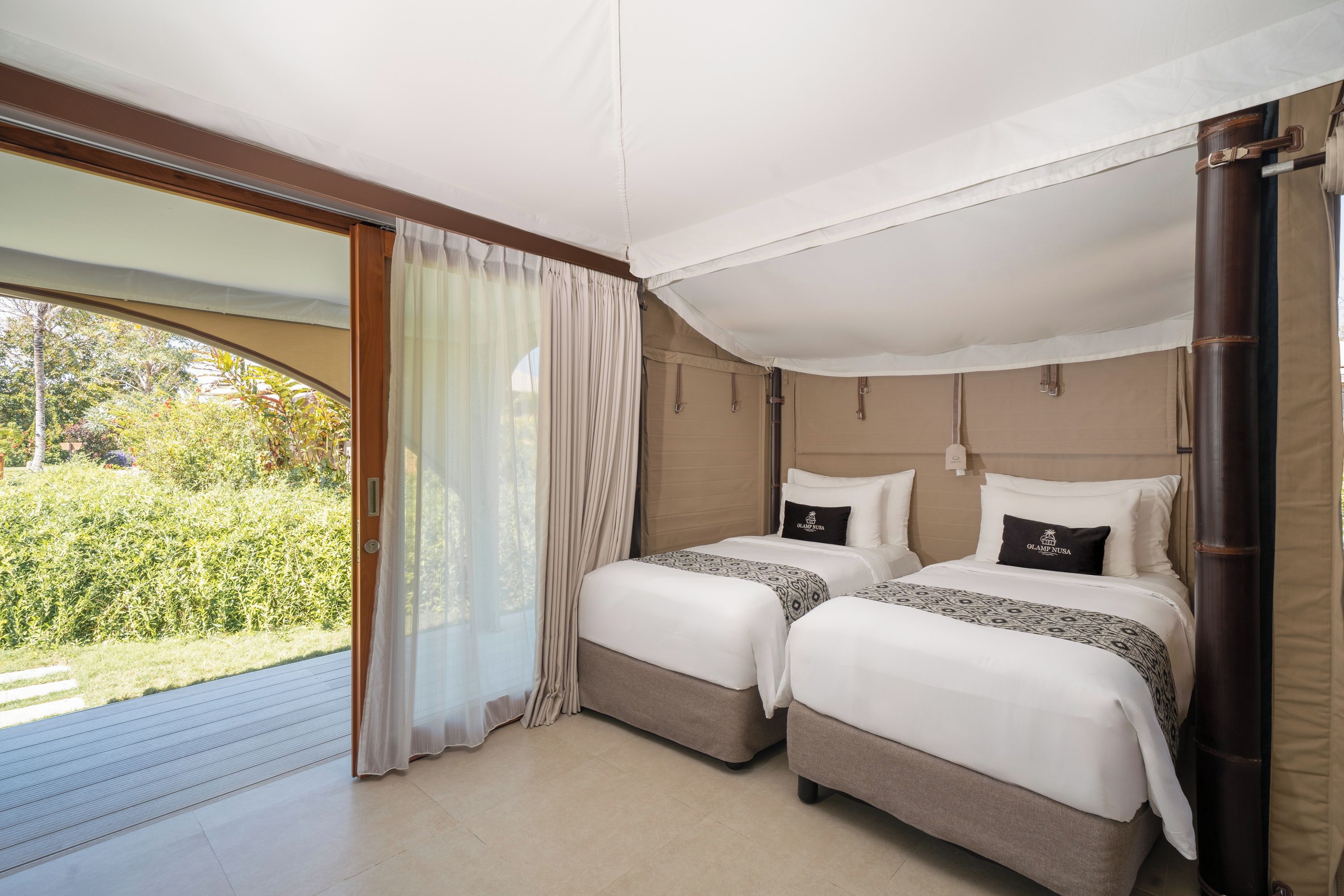 Habitación de hotel con dos camas, un ventanal con cortinas y vistas a zonas verdes.