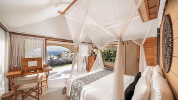 Une chambre à coucher avec un lit à baldaquin, un bureau en bois et une vue sur l’océan.