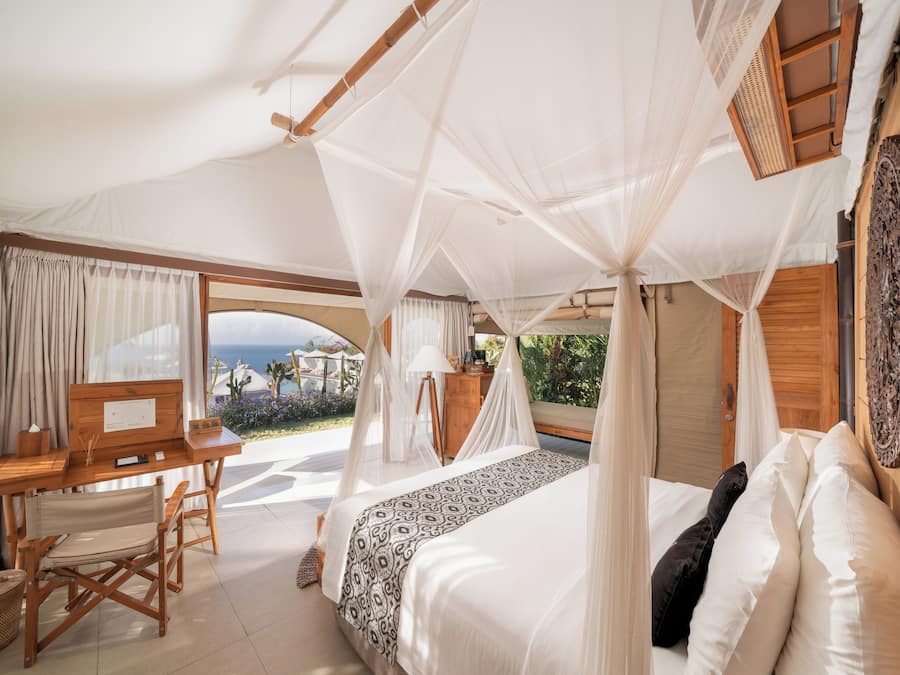 Ein Schlafzimmer mit Baldachinbett, einem Holztisch und Blick aufs Meer.