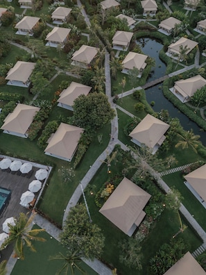 An aerial view of a resort with multiple bungalow-style accommodations, a central water feature, and well-maintained landscaping. - Glamp Nusa (Nusa Dua)