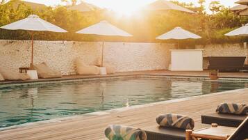 A poolside area with lounge chairs and umbrellas, a stone wall, and a clear view of the pool.