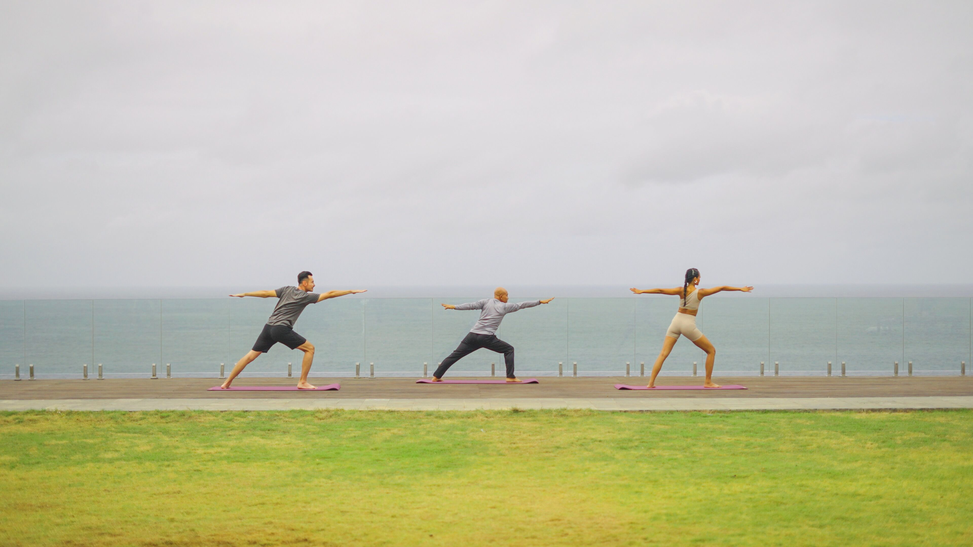 Three people practicing yoga on mats by the sea.