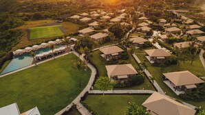 An aerial view of a resort with multiple bungalow-style accommodations, a swimming pool, and well-maintained lawns. - Glamp Nusa (Nusa Dua)
